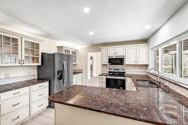 kitchen featuring appliances with stainless steel finishes, sink, white cabinets, dark stone counters, and kitchen peninsula