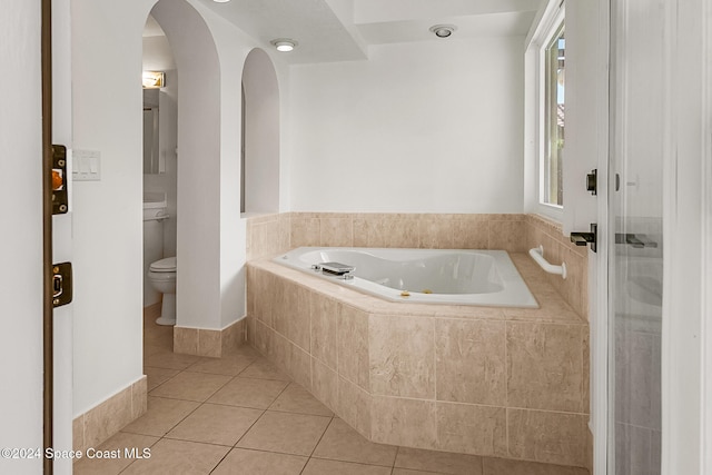 bathroom with a relaxing tiled tub, tile patterned floors, and toilet