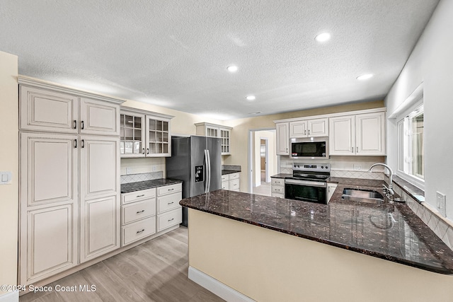 kitchen with sink, stainless steel appliances, light hardwood / wood-style floors, kitchen peninsula, and dark stone counters