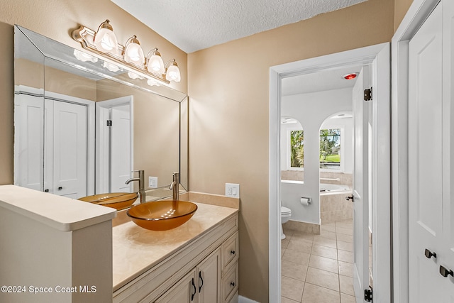 bathroom featuring tiled tub, vanity, a textured ceiling, tile patterned floors, and toilet