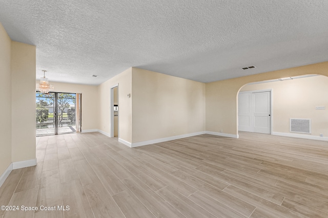 spare room with a notable chandelier, light hardwood / wood-style floors, and a textured ceiling