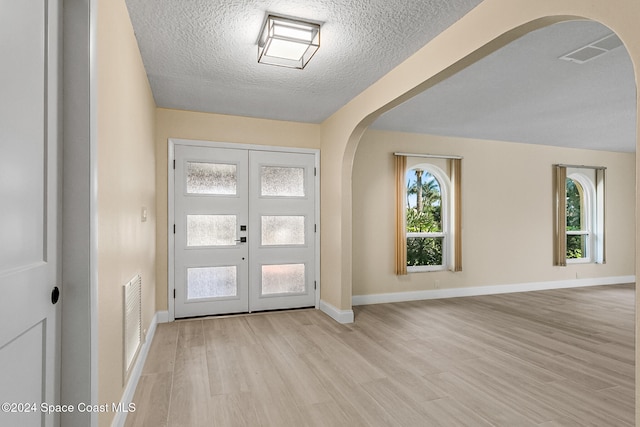 foyer with french doors, a textured ceiling, and light wood-type flooring