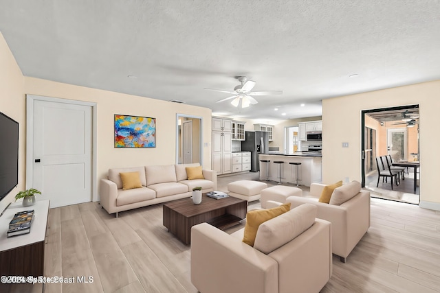 living room with ceiling fan, a textured ceiling, and light wood-type flooring