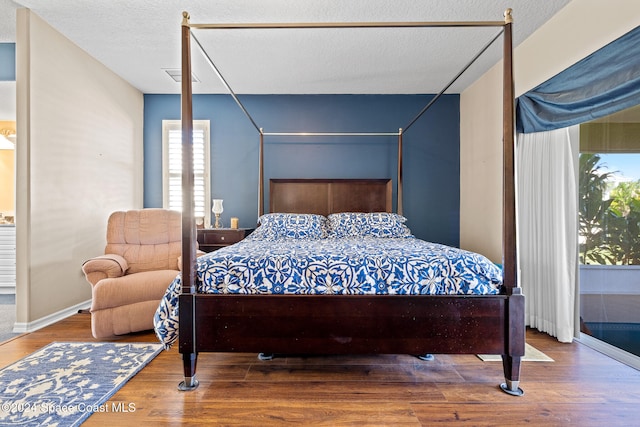 bedroom featuring a textured ceiling, multiple windows, and wood-type flooring