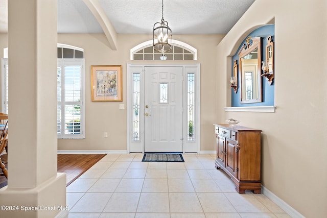 entrance foyer featuring a textured ceiling, beamed ceiling, light tile patterned flooring, and a chandelier