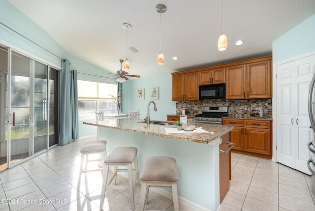 kitchen featuring light stone countertops, gas stove, a kitchen island with sink, sink, and decorative light fixtures