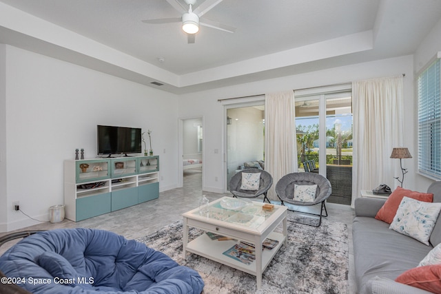 living room with a raised ceiling and ceiling fan