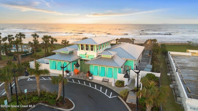 aerial view at dusk featuring a water view and a view of the beach