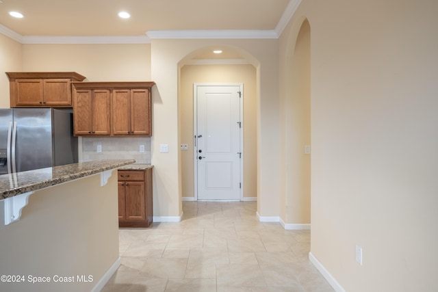 kitchen featuring brown cabinets, stainless steel fridge, dark stone countertops, recessed lighting, and ornamental molding