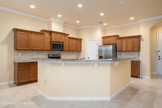 kitchen with brown cabinets, appliances with stainless steel finishes, a large island with sink, and a breakfast bar area