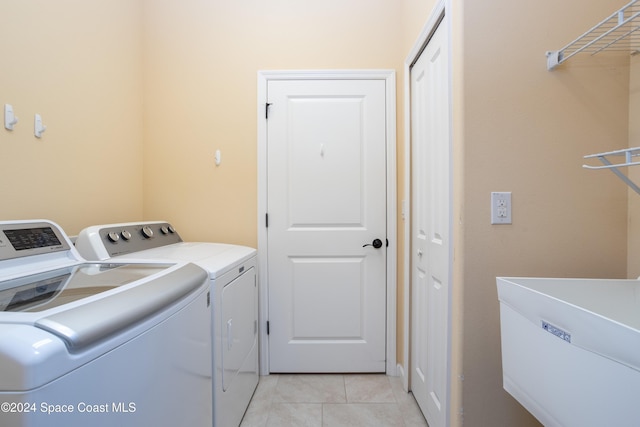washroom with light tile patterned flooring, laundry area, washing machine and dryer, and a sink
