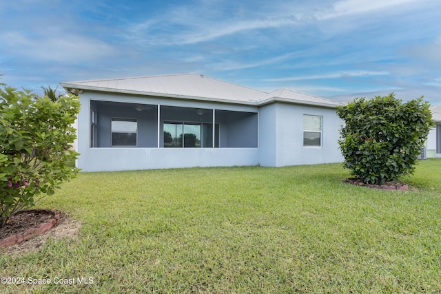 rear view of property featuring a lawn, metal roof, a sunroom, and stucco siding