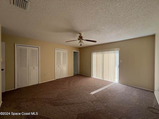 unfurnished bedroom with ceiling fan, carpet floors, a textured ceiling, and multiple closets