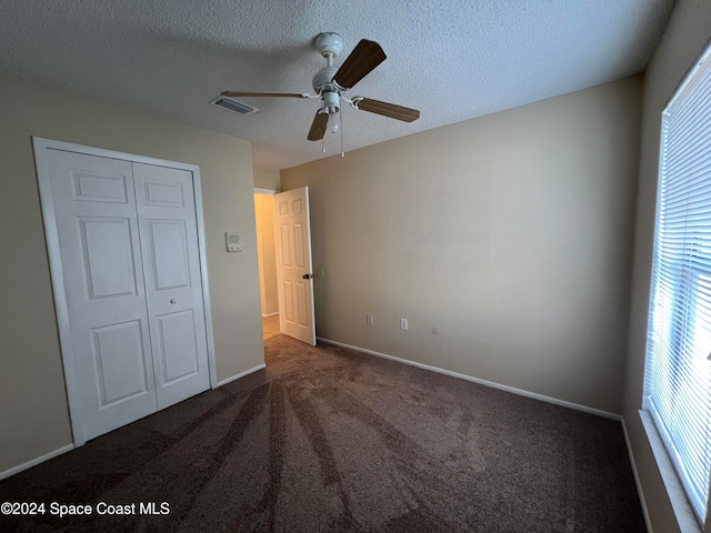 unfurnished bedroom with ceiling fan, a closet, dark carpet, and multiple windows