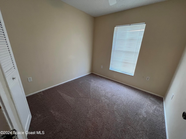 unfurnished room with dark colored carpet and a textured ceiling