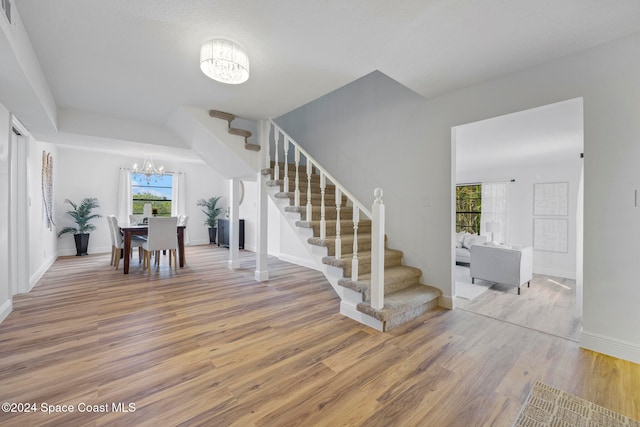 stairs with hardwood / wood-style floors and a notable chandelier