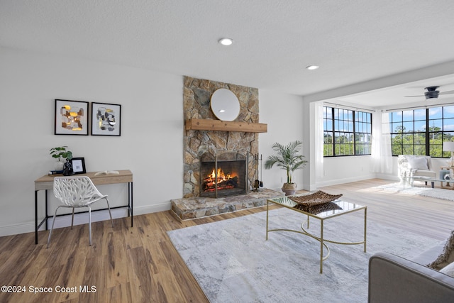 living room featuring ceiling fan, hardwood / wood-style flooring, a stone fireplace, and a textured ceiling