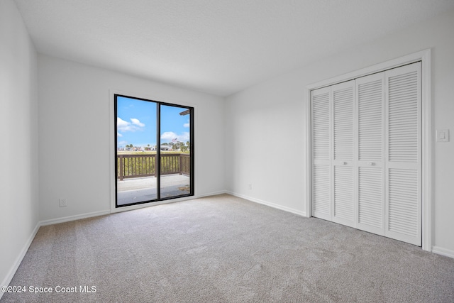 unfurnished bedroom featuring access to exterior, a closet, and light colored carpet