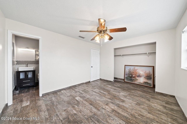 unfurnished bedroom with a textured ceiling, ceiling fan, dark wood-type flooring, and sink