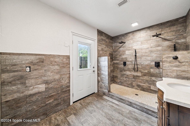 bathroom with a tile shower, hardwood / wood-style floors, vanity, and tile walls