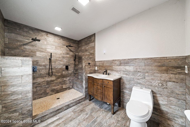 bathroom featuring a tile shower, hardwood / wood-style floors, toilet, vanity, and tile walls