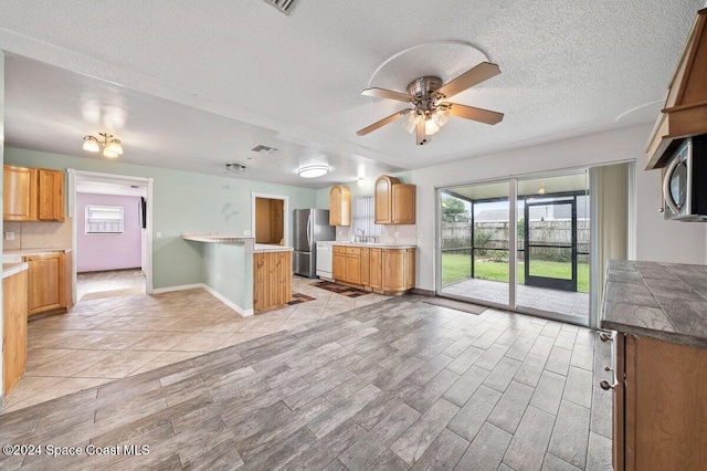 kitchen featuring ceiling fan, light wood-type flooring, a textured ceiling, and appliances with stainless steel finishes