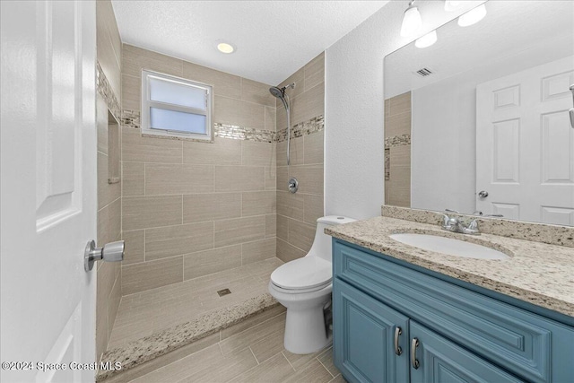 bathroom with vanity, toilet, a textured ceiling, and a tile shower