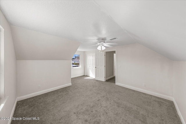 additional living space with ceiling fan, a textured ceiling, vaulted ceiling, and dark carpet