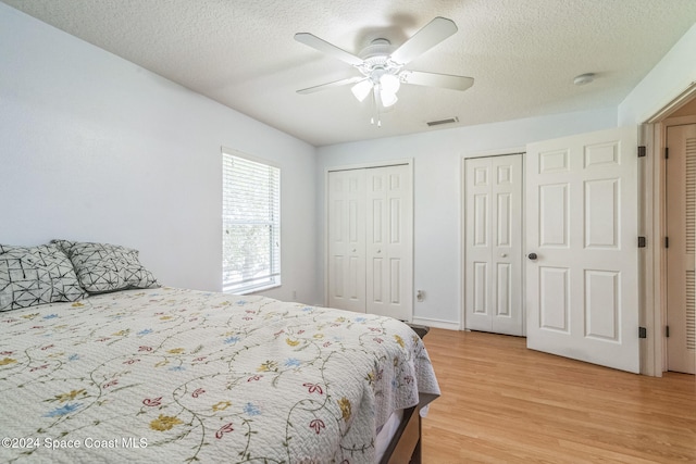 bedroom with light hardwood / wood-style flooring, two closets, a textured ceiling, and ceiling fan