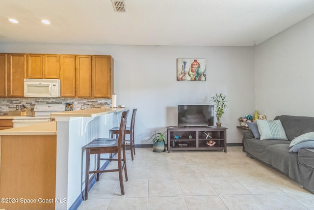 kitchen with a kitchen breakfast bar, kitchen peninsula, backsplash, light tile patterned flooring, and white appliances