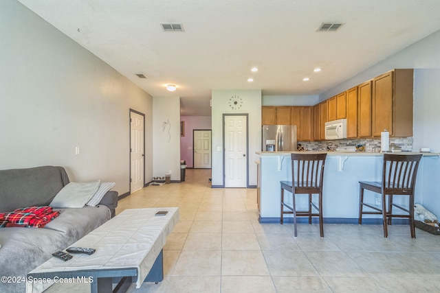 kitchen featuring tasteful backsplash, kitchen peninsula, a breakfast bar area, stainless steel fridge with ice dispenser, and light tile patterned floors