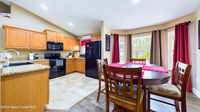 kitchen with light stone countertops, black appliances, sink, light hardwood / wood-style floors, and vaulted ceiling