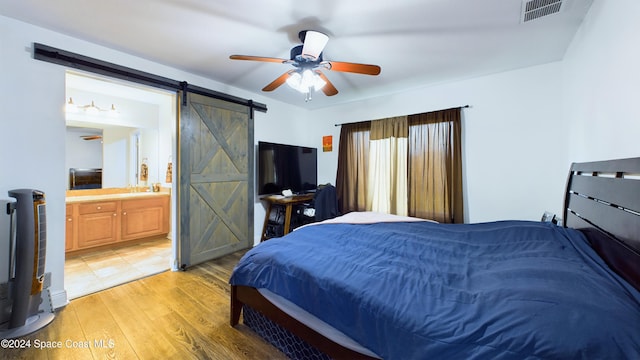 bedroom with ensuite bath, light wood-type flooring, a barn door, and ceiling fan