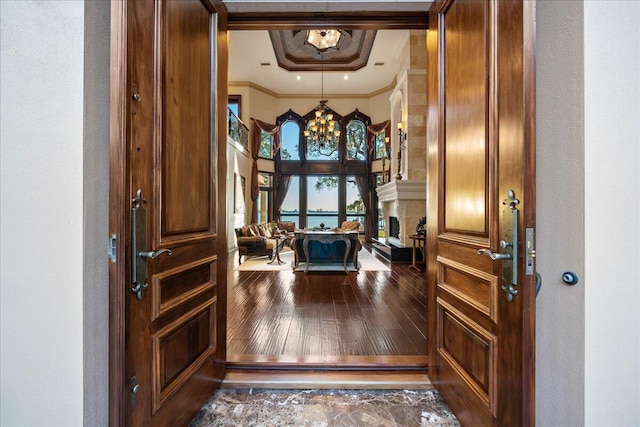 foyer entrance with a tray ceiling, dark wood-type flooring, crown molding, and an inviting chandelier