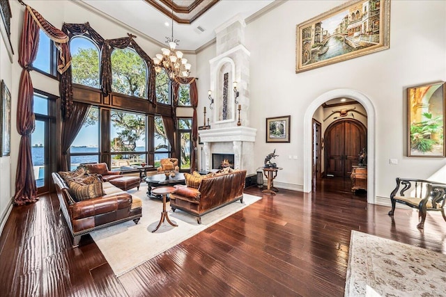 living room with a high ceiling, a large fireplace, ornamental molding, a water view, and dark hardwood / wood-style flooring