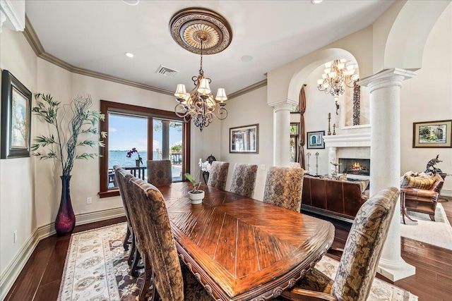 dining space with ornate columns, ornamental molding, an inviting chandelier, a water view, and dark hardwood / wood-style flooring