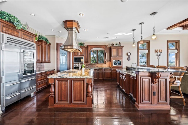 kitchen with a spacious island, dark wood-type flooring, crown molding, decorative light fixtures, and appliances with stainless steel finishes