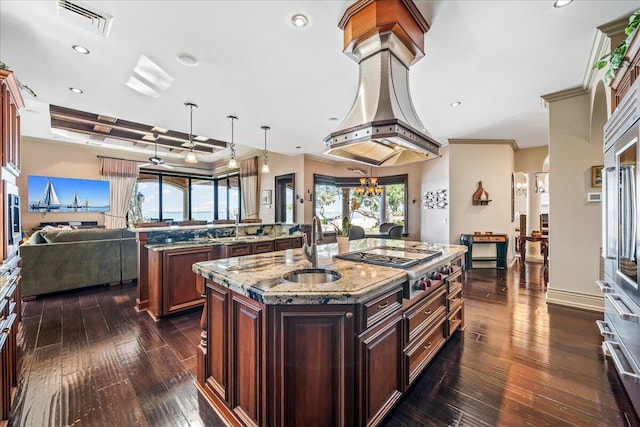 kitchen featuring crown molding, sink, dark wood-type flooring, light stone counters, and a center island with sink