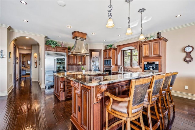 kitchen featuring a spacious island, decorative light fixtures, built in appliances, and dark hardwood / wood-style flooring