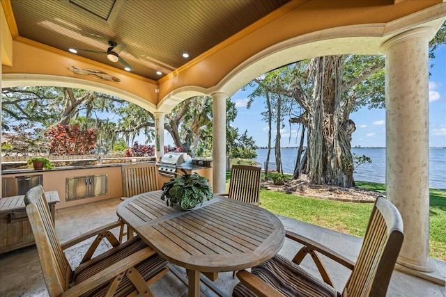 view of patio with an outdoor kitchen, grilling area, a water view, and ceiling fan