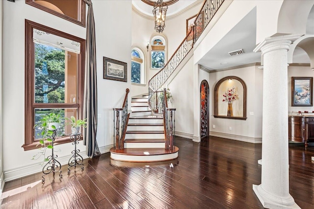 entrance foyer featuring a towering ceiling, dark wood-type flooring, and ornate columns