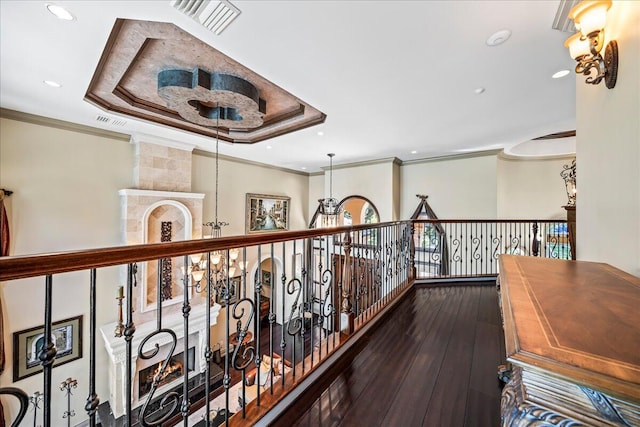 hallway featuring a raised ceiling, ornamental molding, an inviting chandelier, and dark hardwood / wood-style floors