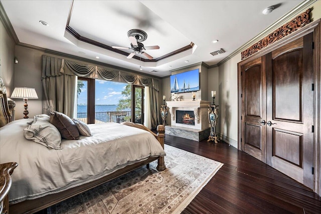 bedroom featuring a tray ceiling, ornamental molding, ceiling fan, a fireplace, and dark hardwood / wood-style flooring