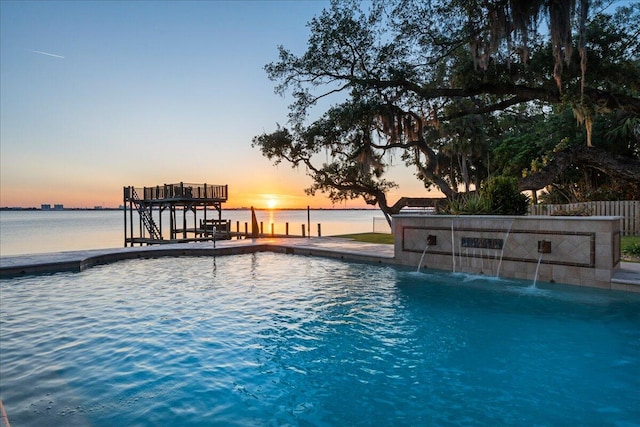 pool at dusk featuring pool water feature and a water view