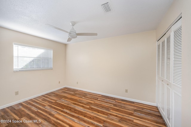 unfurnished bedroom featuring ceiling fan, a closet, a textured ceiling, and dark hardwood / wood-style flooring