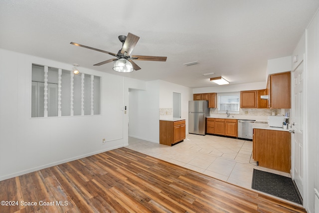 kitchen with tasteful backsplash, light wood-type flooring, stainless steel appliances, ceiling fan, and sink