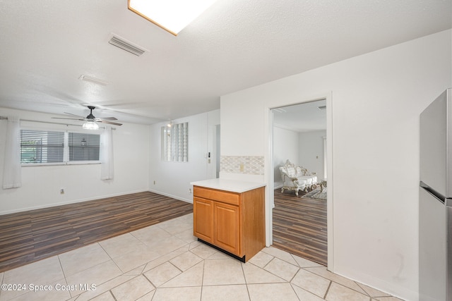 kitchen with a textured ceiling, ceiling fan, decorative backsplash, stainless steel fridge, and light tile patterned floors