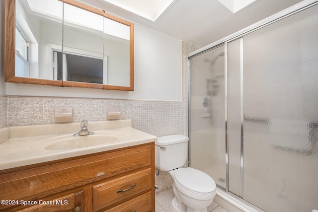 bathroom with a shower with shower door, tile walls, vanity, toilet, and tile patterned floors