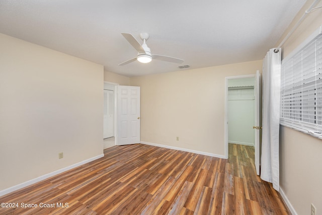 unfurnished bedroom featuring ceiling fan, a closet, dark wood-type flooring, and a spacious closet