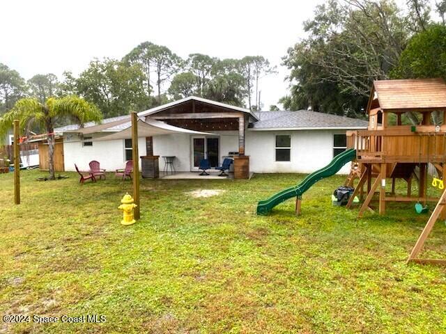 rear view of property with a playground, a patio area, and a lawn